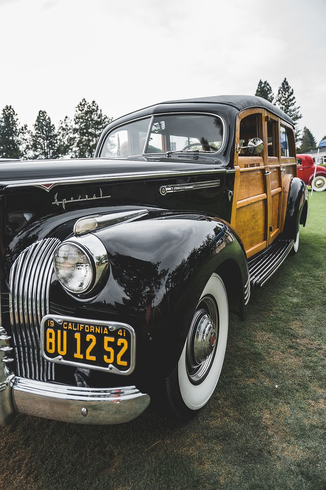 A black and wooden vintage car with a california license plate is parked on the grass.