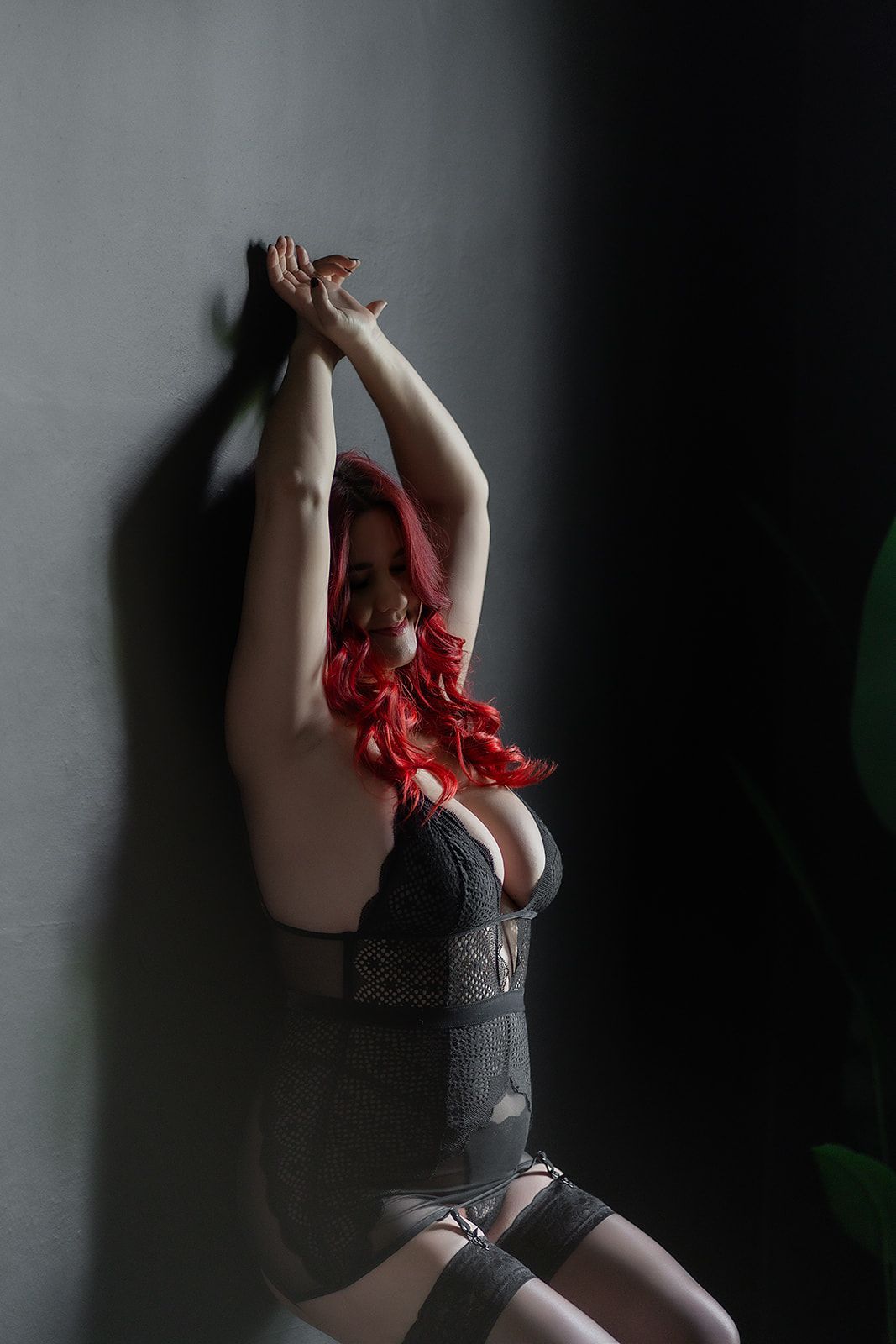 A woman with red hair is sitting in front of a wall with her arms up.