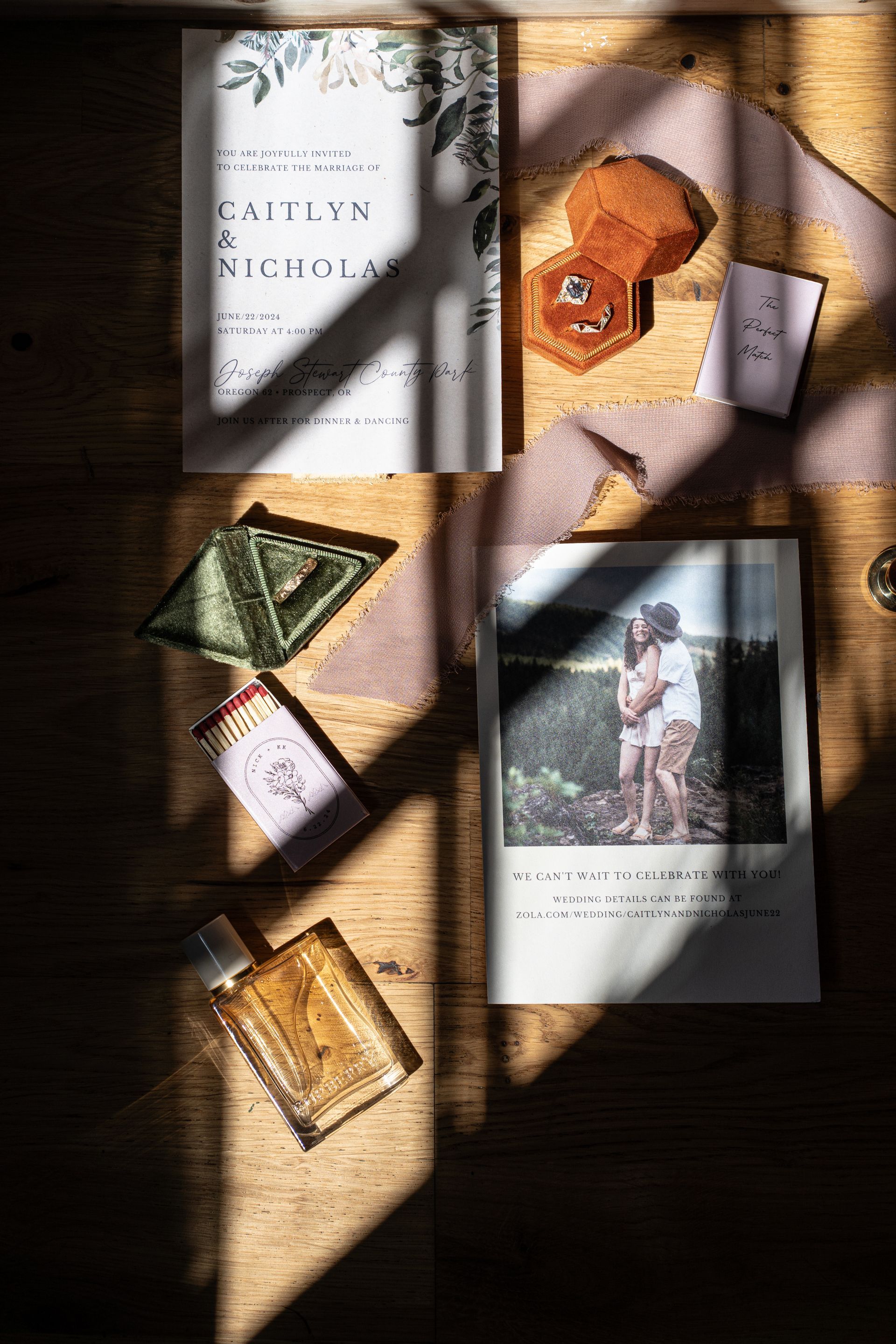 A wedding invitation , rings , perfume , and other wedding decorations are sitting on a wooden table.
