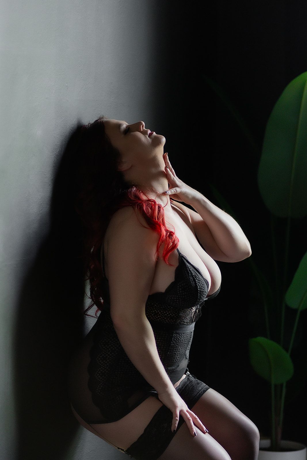 A woman with red hair is standing in front of a black wall.