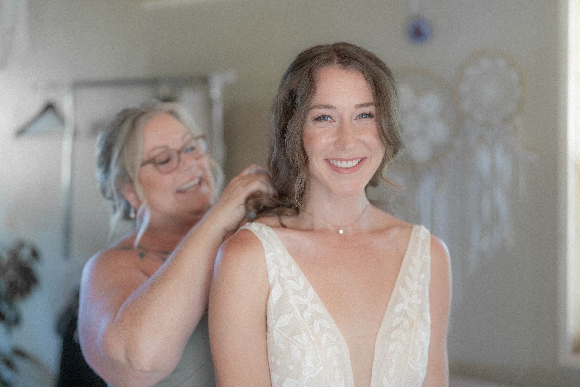 A woman is putting a necklace on a bride 's neck.