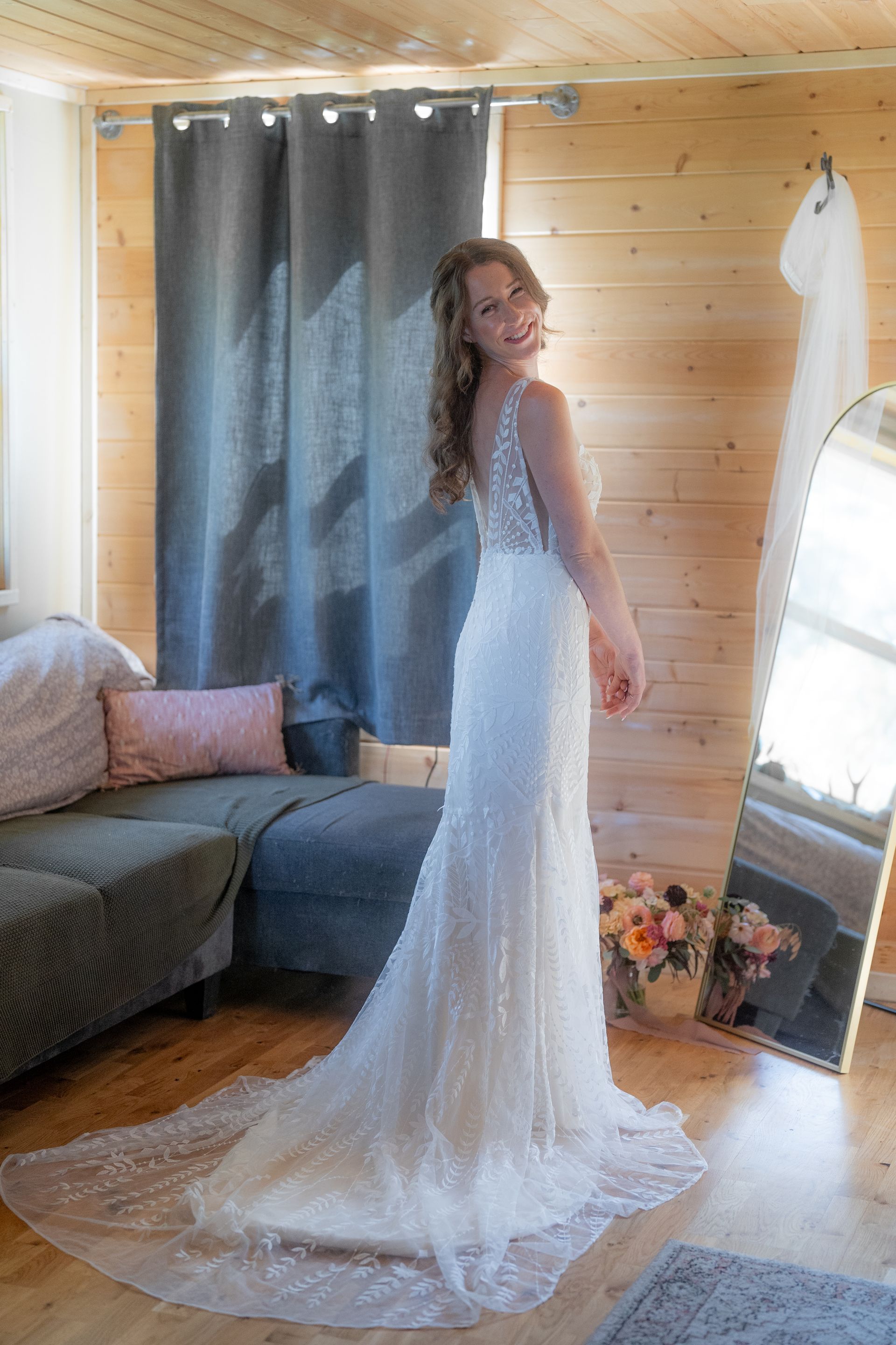 A woman in a wedding dress is standing in front of a mirror in a room.