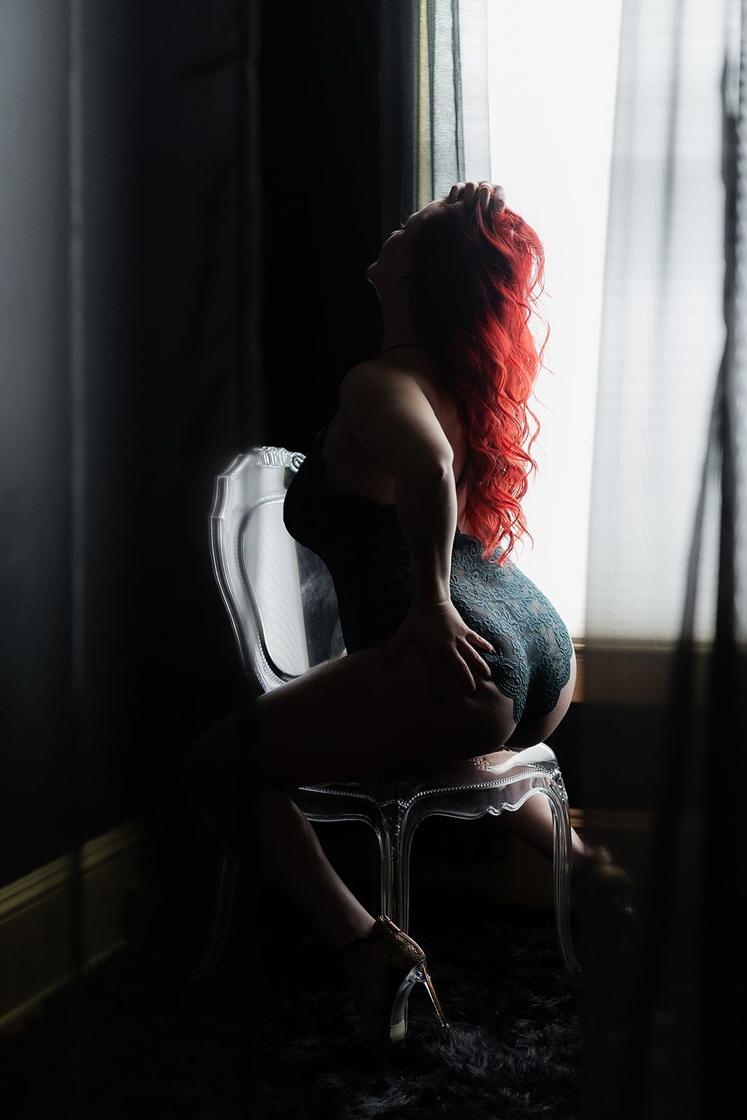 A woman with red hair is sitting in a chair in front of a window.