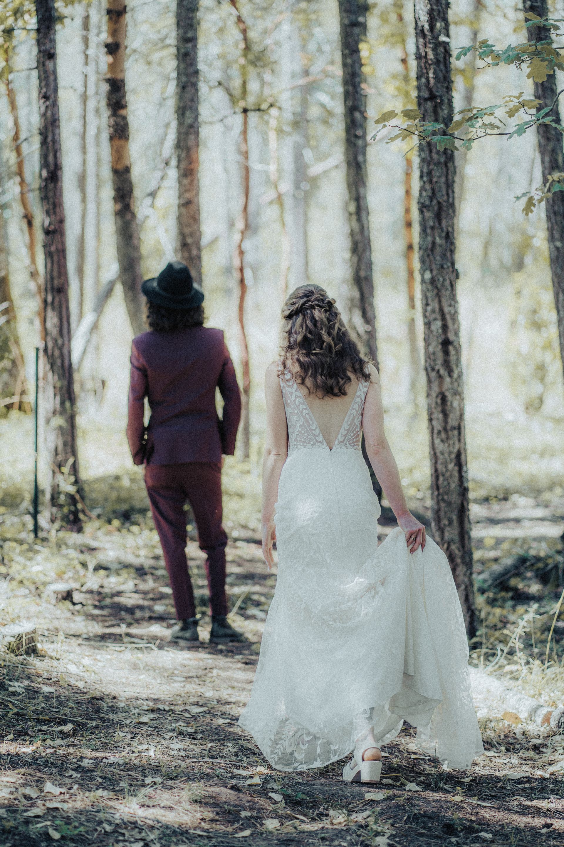 A bride and groom are walking through a forest.
