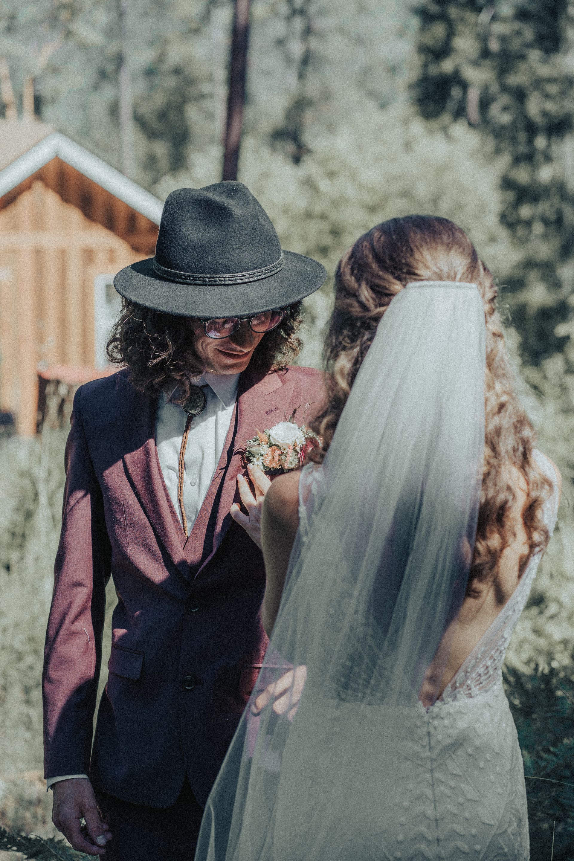 A man in a suit and hat is standing next to a woman in a wedding dress and veil.