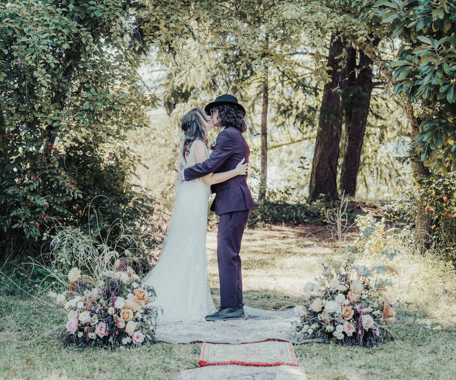 A bride and groom are kissing during their wedding ceremony in the woods.
