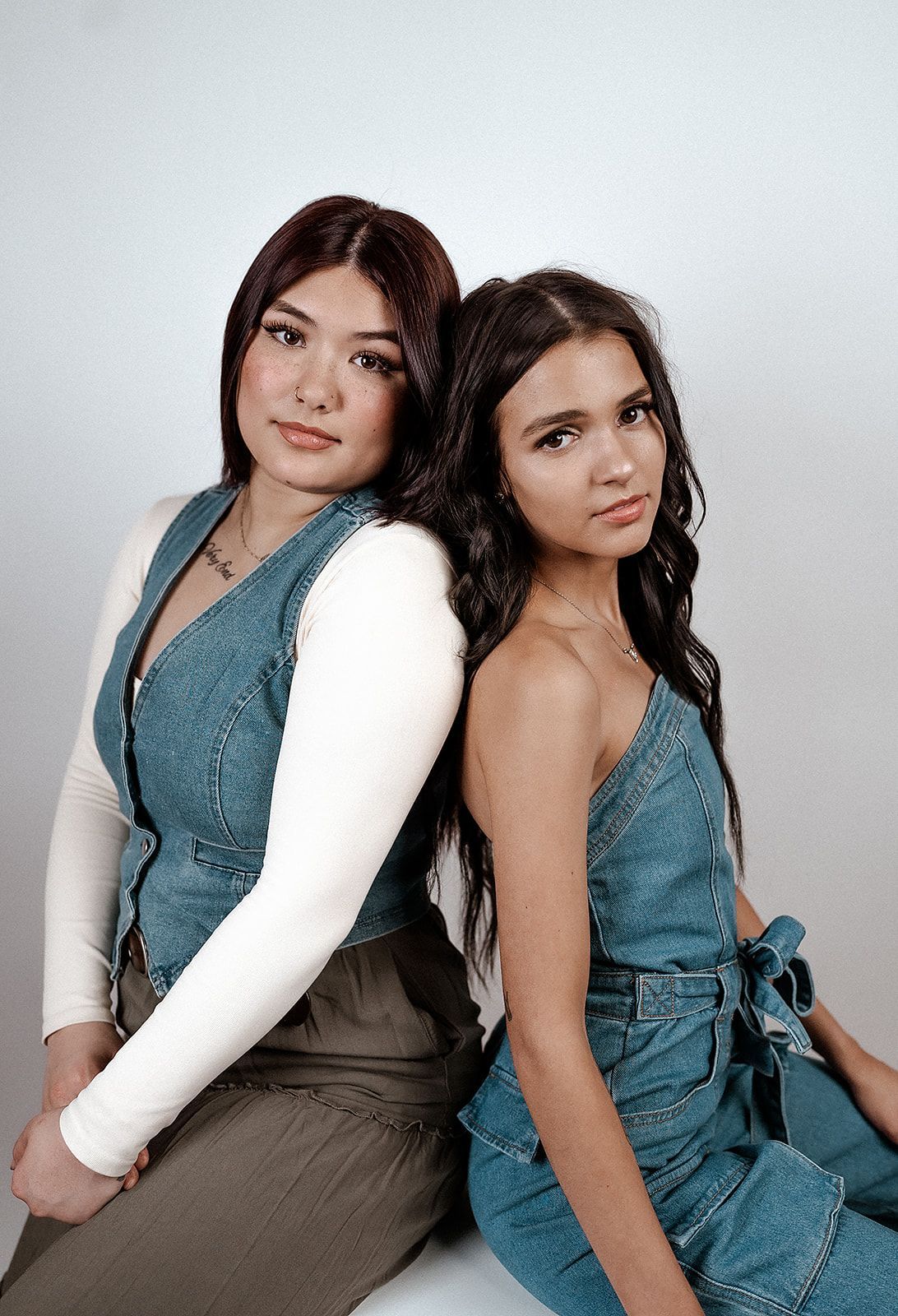 Two young women are sitting back to back and posing for a picture.