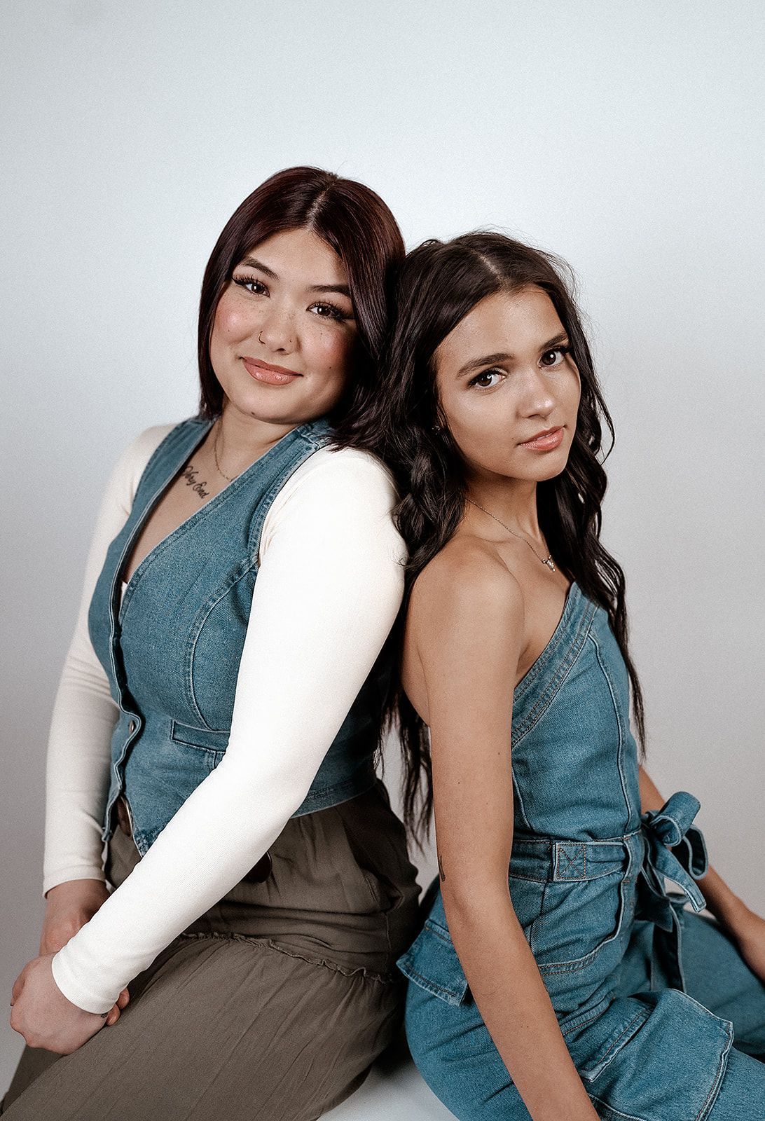 Two women are sitting back to back and posing for a picture.