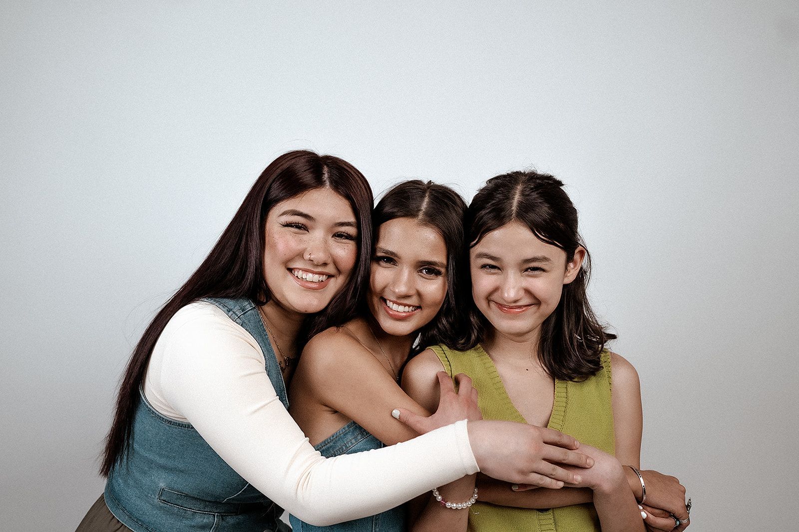 Three young women are hugging each other and smiling for the camera.