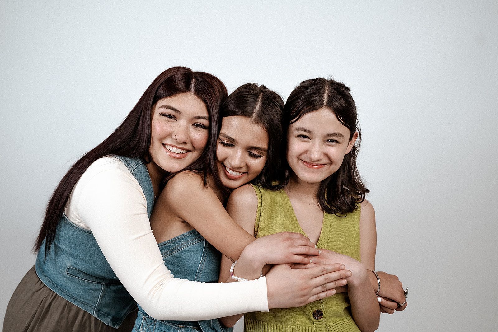 Three young women are hugging each other and smiling for the camera.