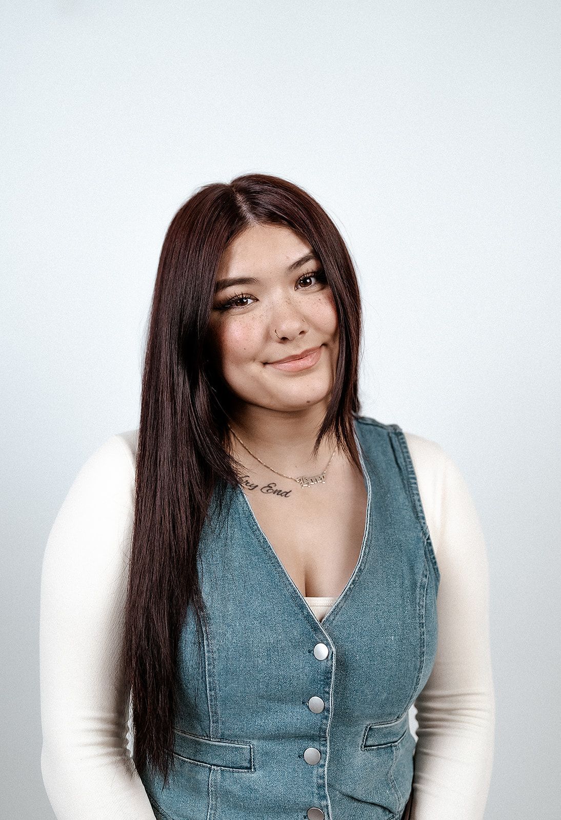 A woman wearing a denim vest and a necklace is smiling for the camera.