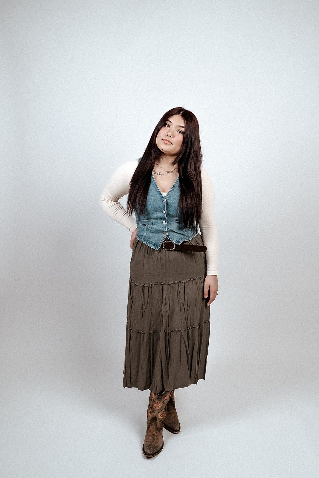 A woman in a skirt and boots is standing in front of a white wall.