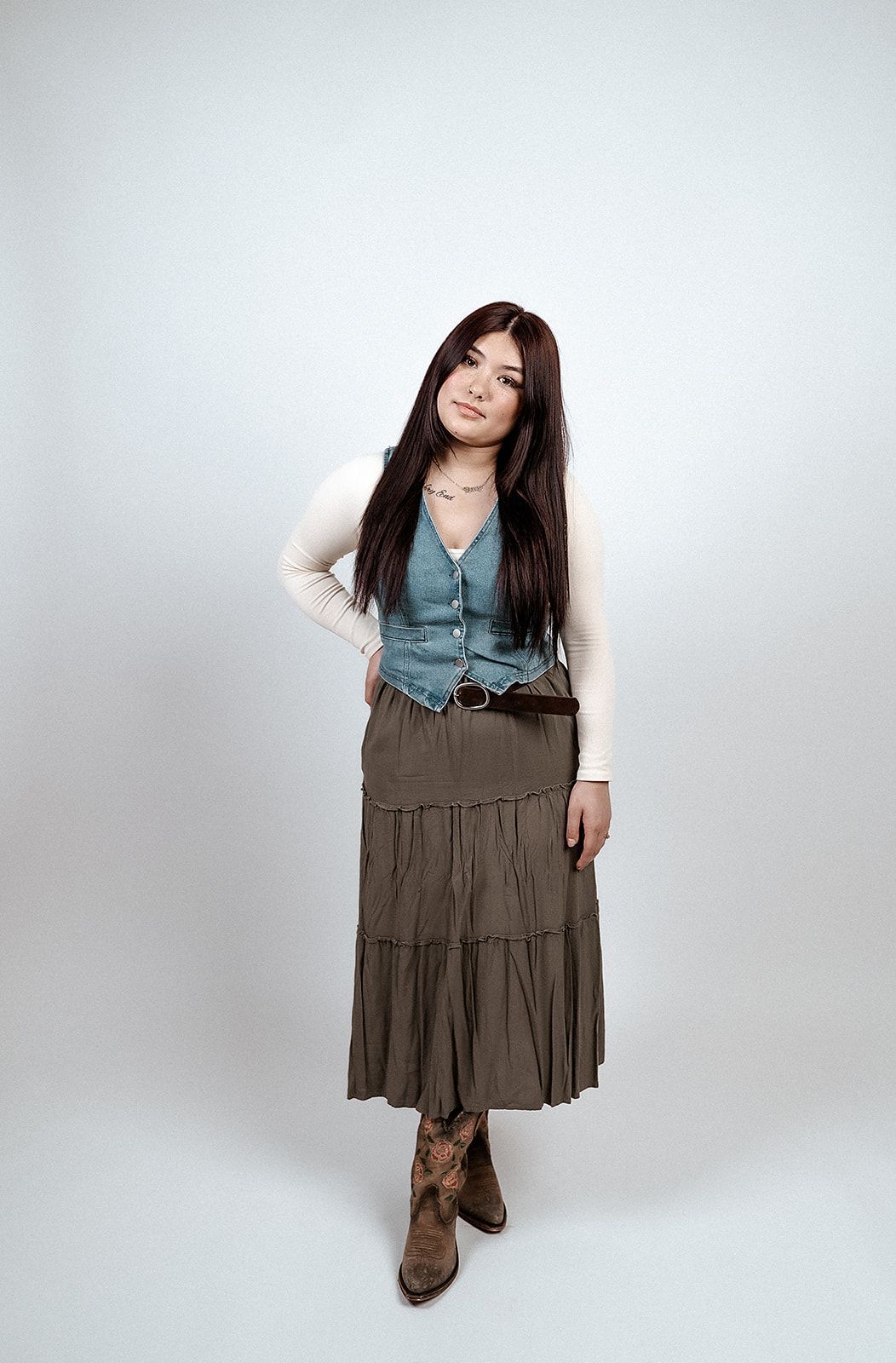 A woman in a skirt and boots is standing in front of a white background.