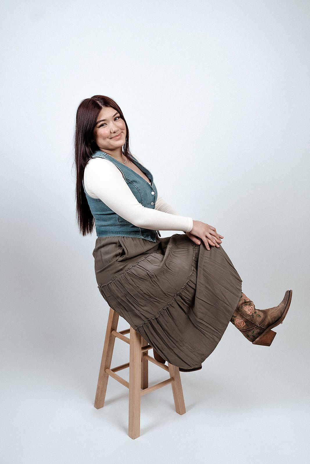 A woman is sitting on a wooden stool with her legs crossed.