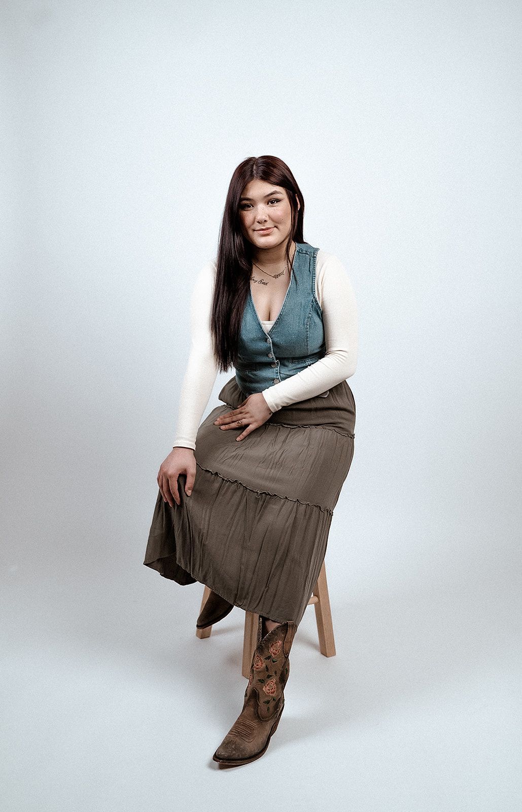 A woman is sitting on a stool wearing a skirt and boots.