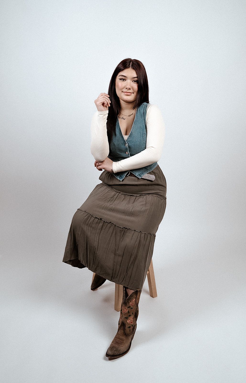 A woman is sitting on a stool wearing a skirt and cowboy boots.