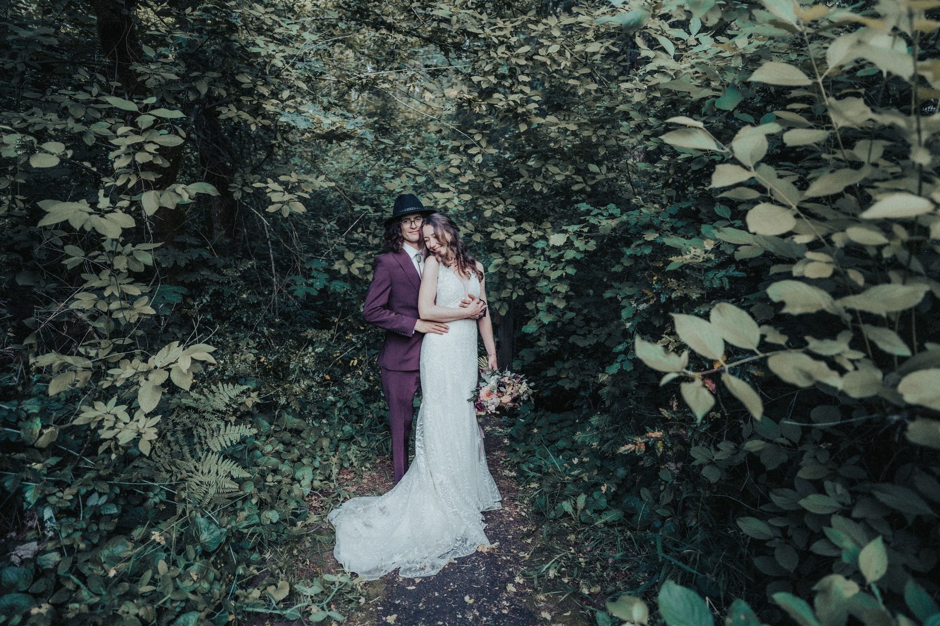A bride and groom are posing for a picture in the woods.