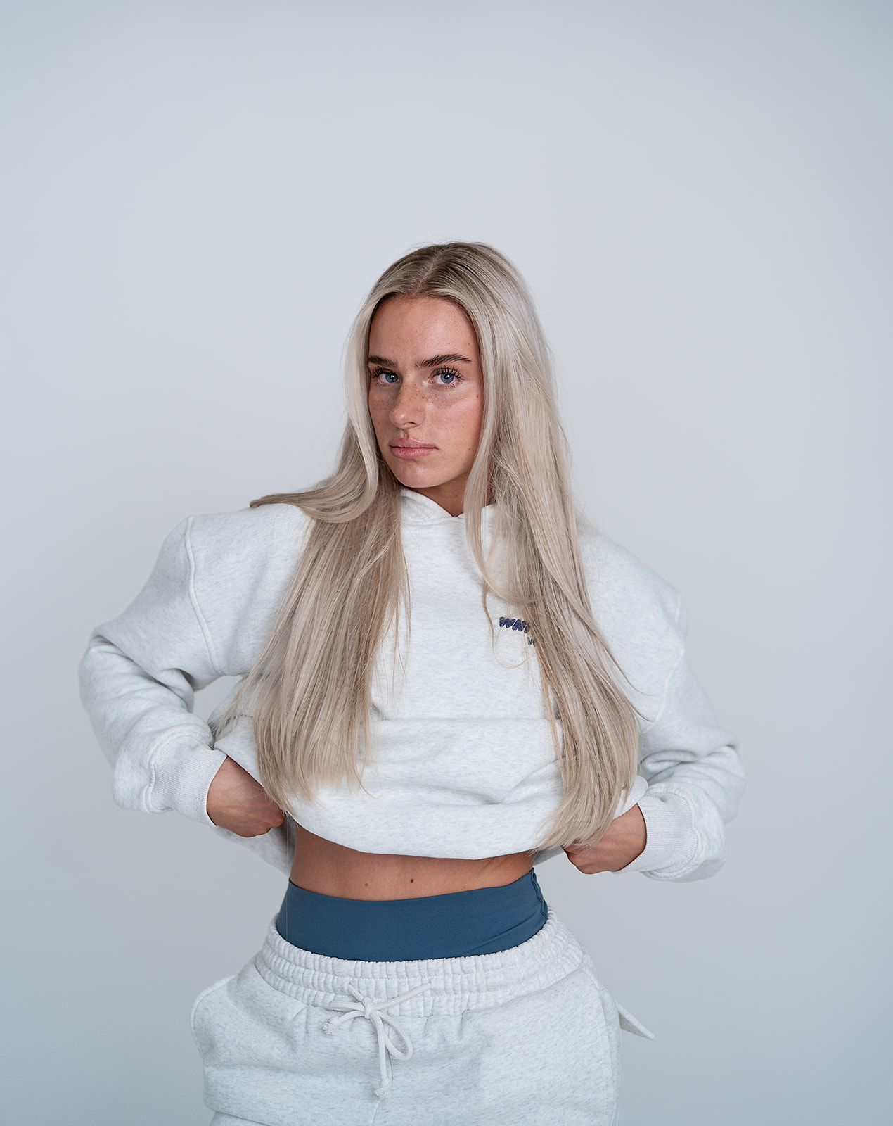 A woman is wearing a white crop top and grey sweatpants.