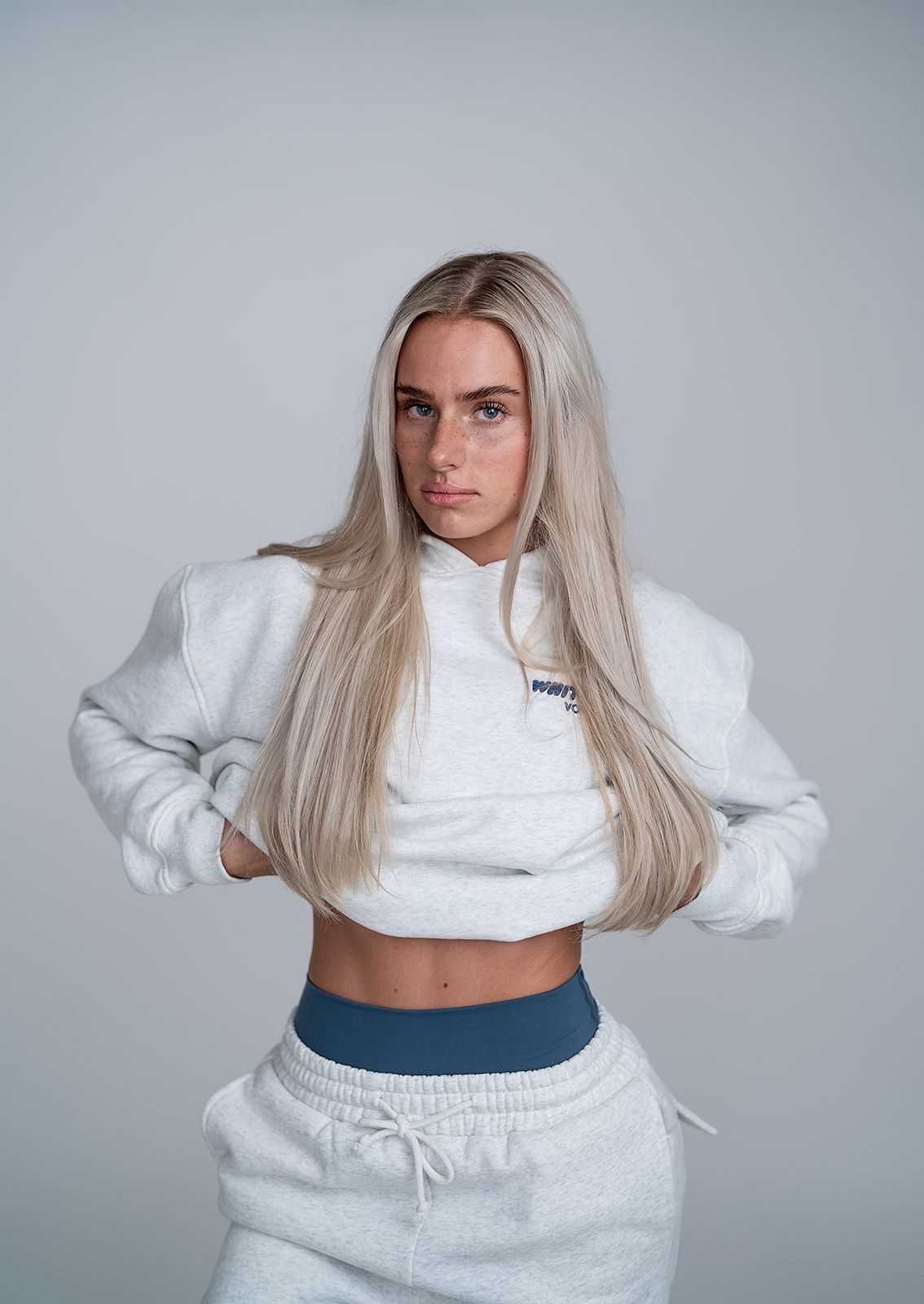 A woman is wearing a white crop top and white sweatpants.