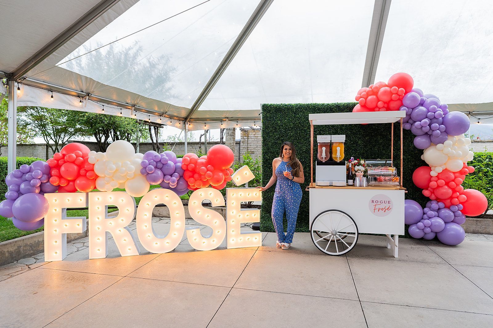 A woman is standing in front of a cart decorated with balloons and a large sign that says frose.