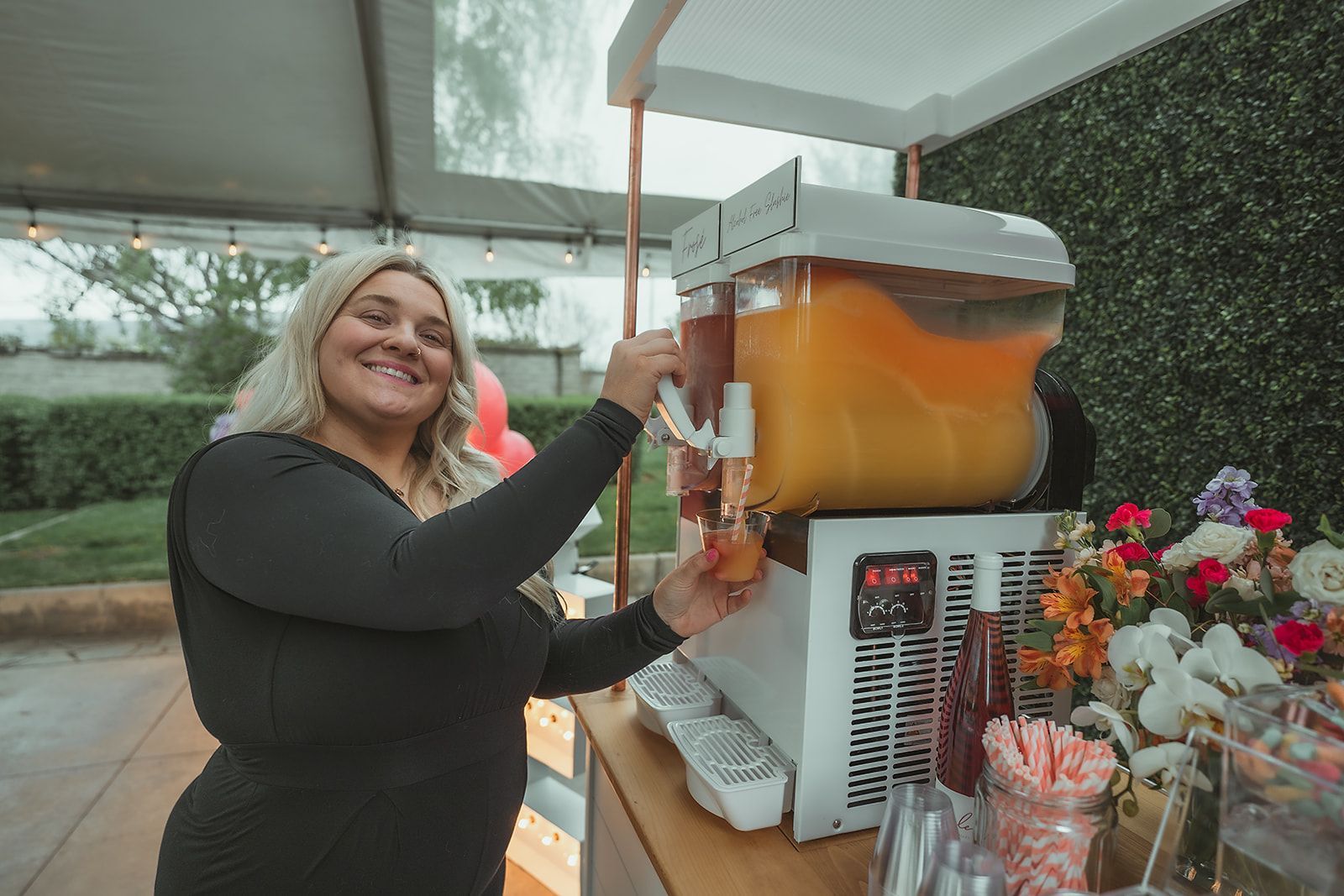 A woman is pouring orange juice into a drink dispenser.