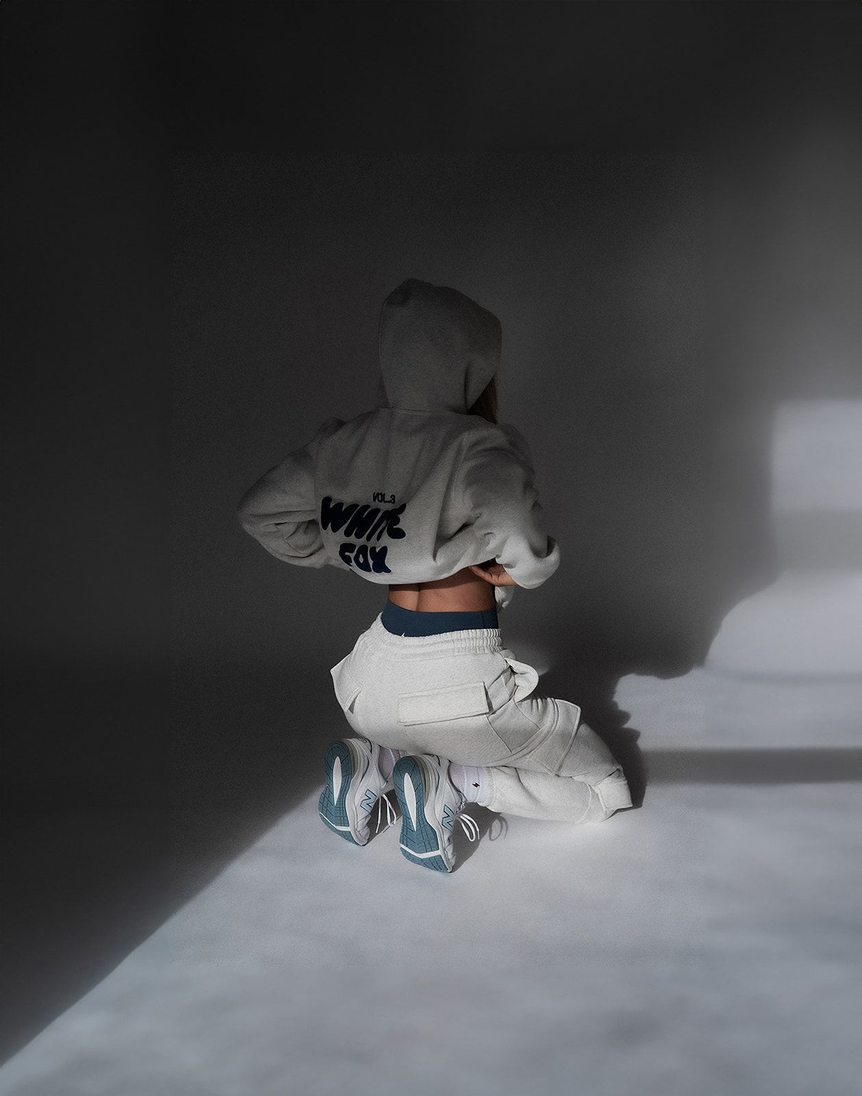 A woman is kneeling down wearing a white hoodie and white pants.