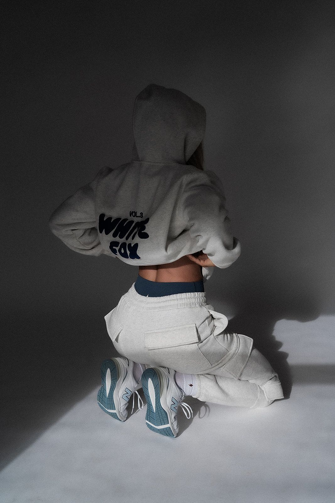 A woman is kneeling down wearing a white hoodie and white sweatpants.