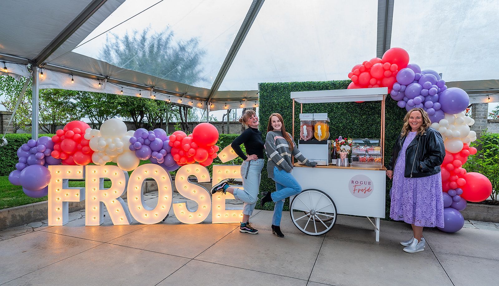 Two women are standing in front of a cart decorated with balloons.