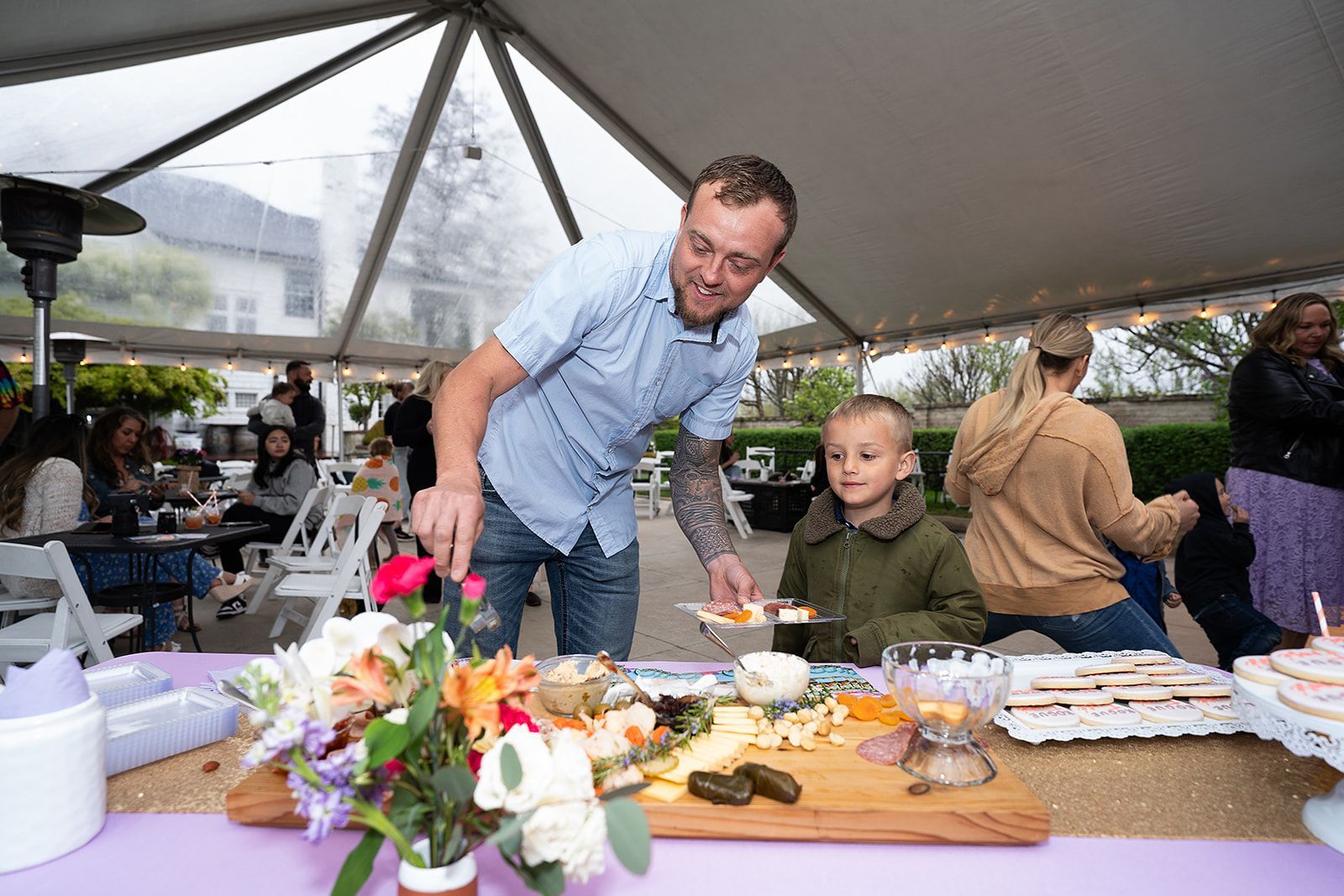 A man is serving food to a young boy at a party under a tent.