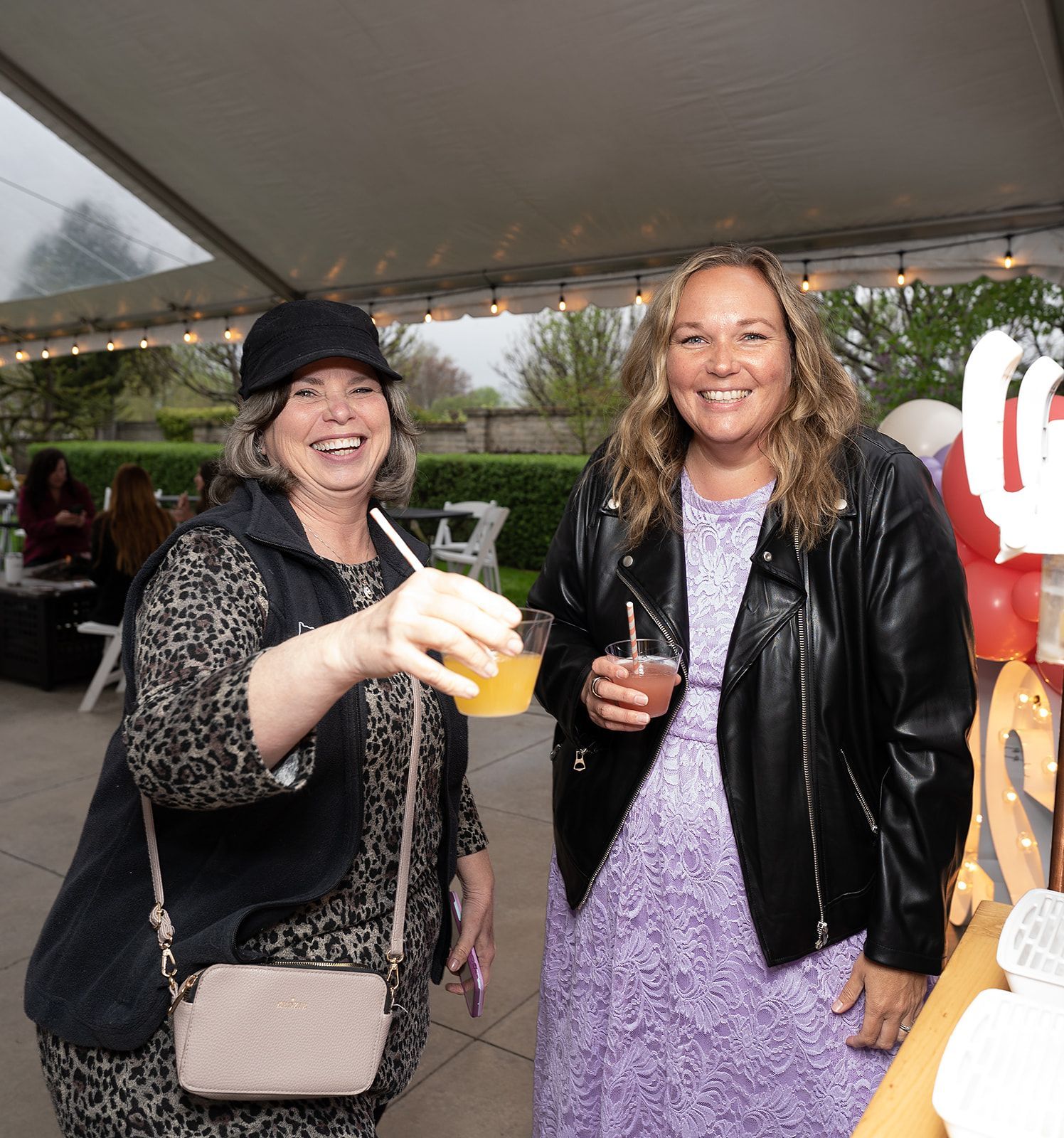 Two women standing next to each other holding drinks and smiling