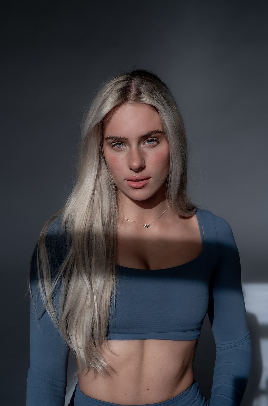 A woman in a blue crop top is standing in front of a wall.