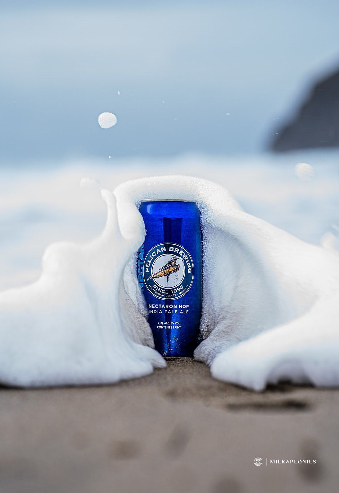 A blue can of beer is covered in snow on the beach.