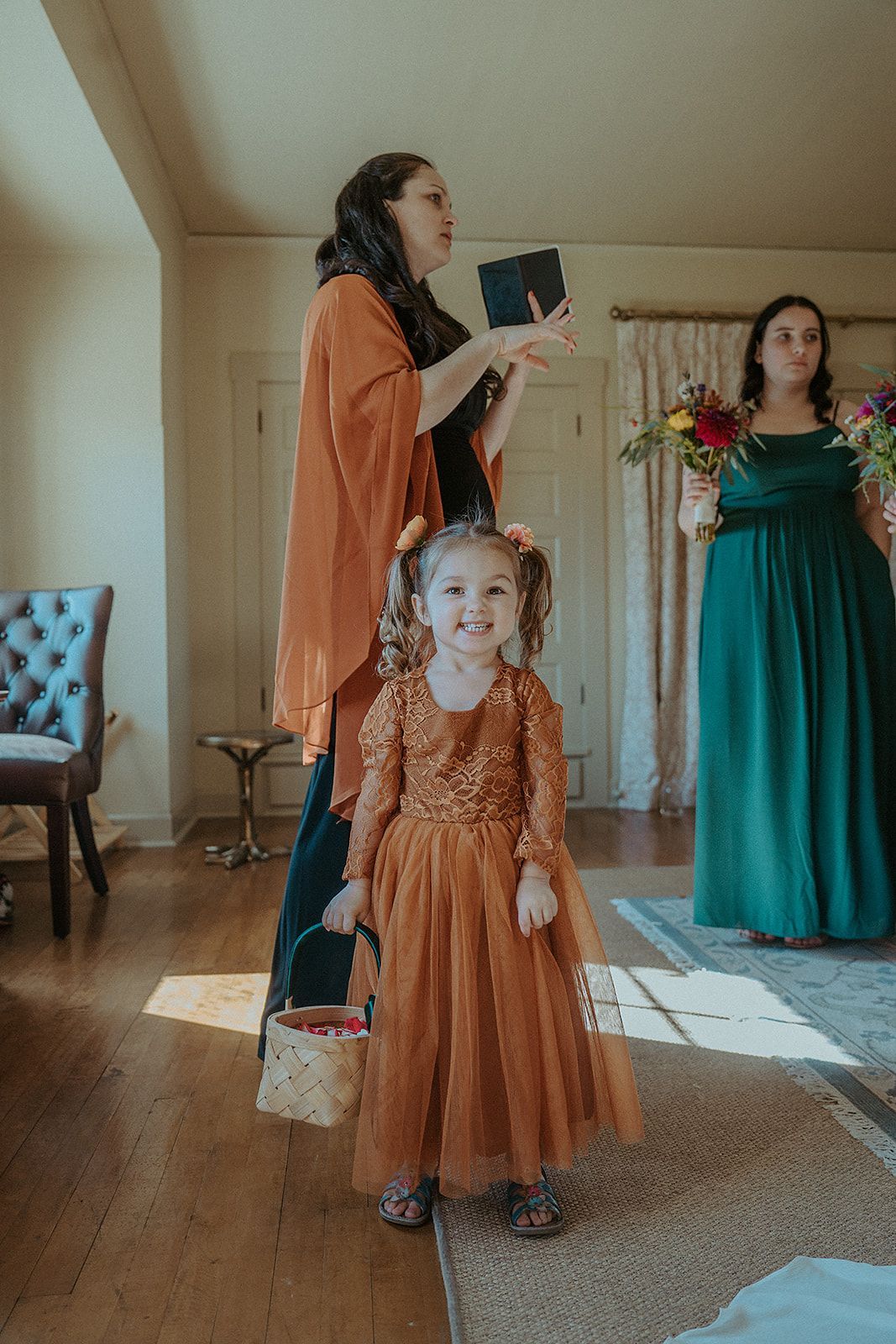 A little girl in a flower girl dress is standing next to a woman in a green dress.