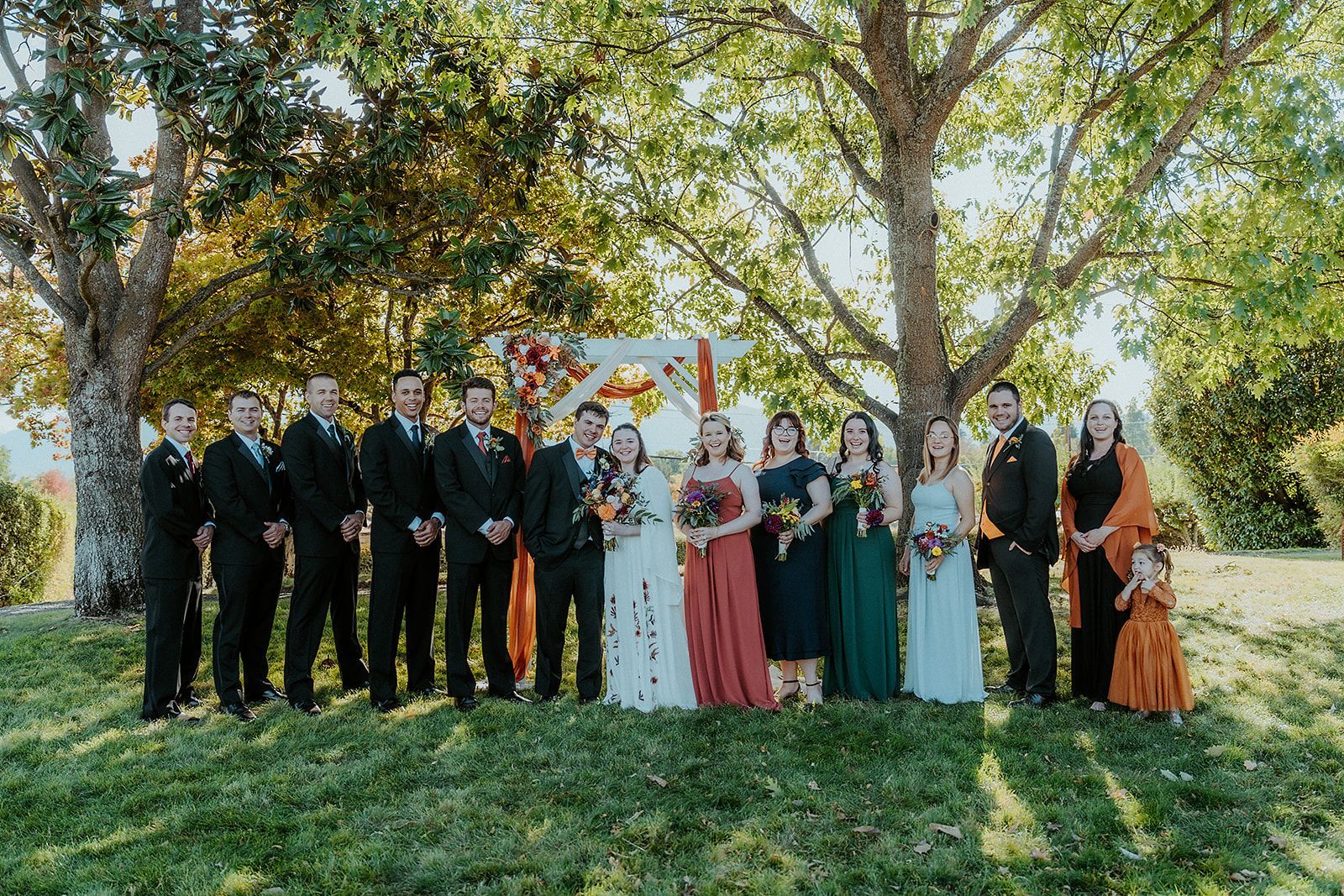 A wedding party is standing next to each other in a field.