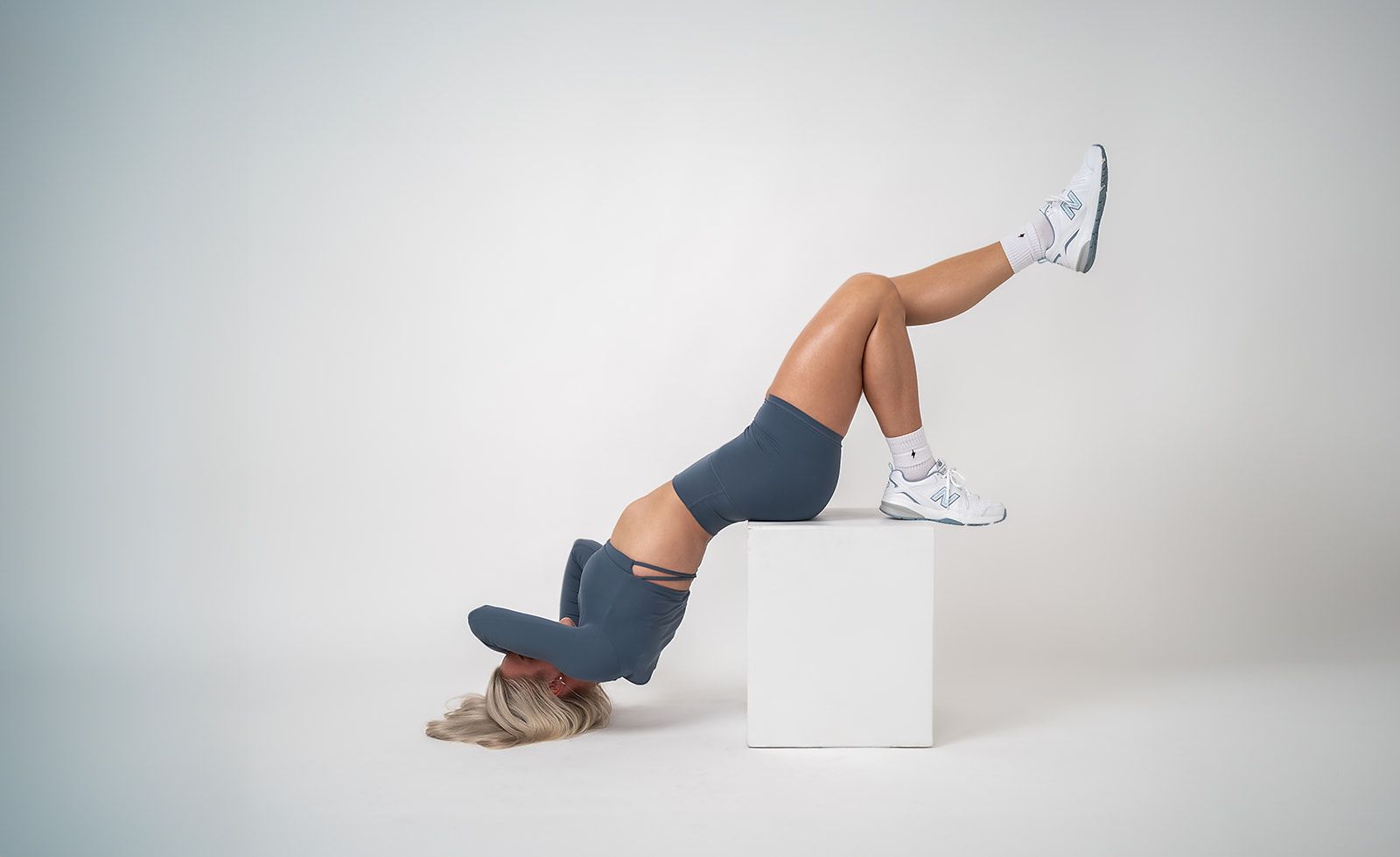 A woman is sitting on a white cube with her legs up.