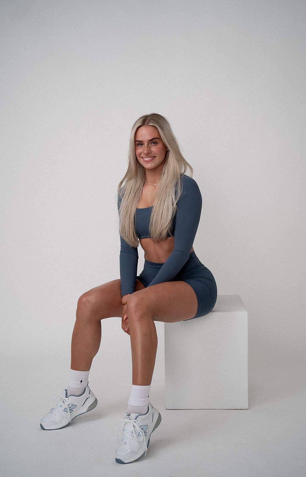 A woman is sitting on a white cube with her legs crossed.