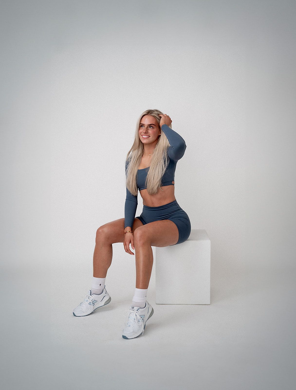 A woman in a crop top and shorts is sitting on a white box.