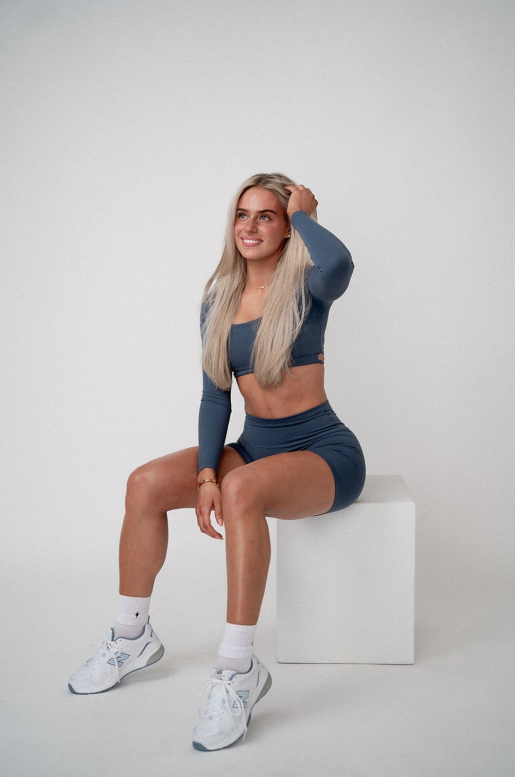 A woman is sitting on a white cube with her legs crossed.