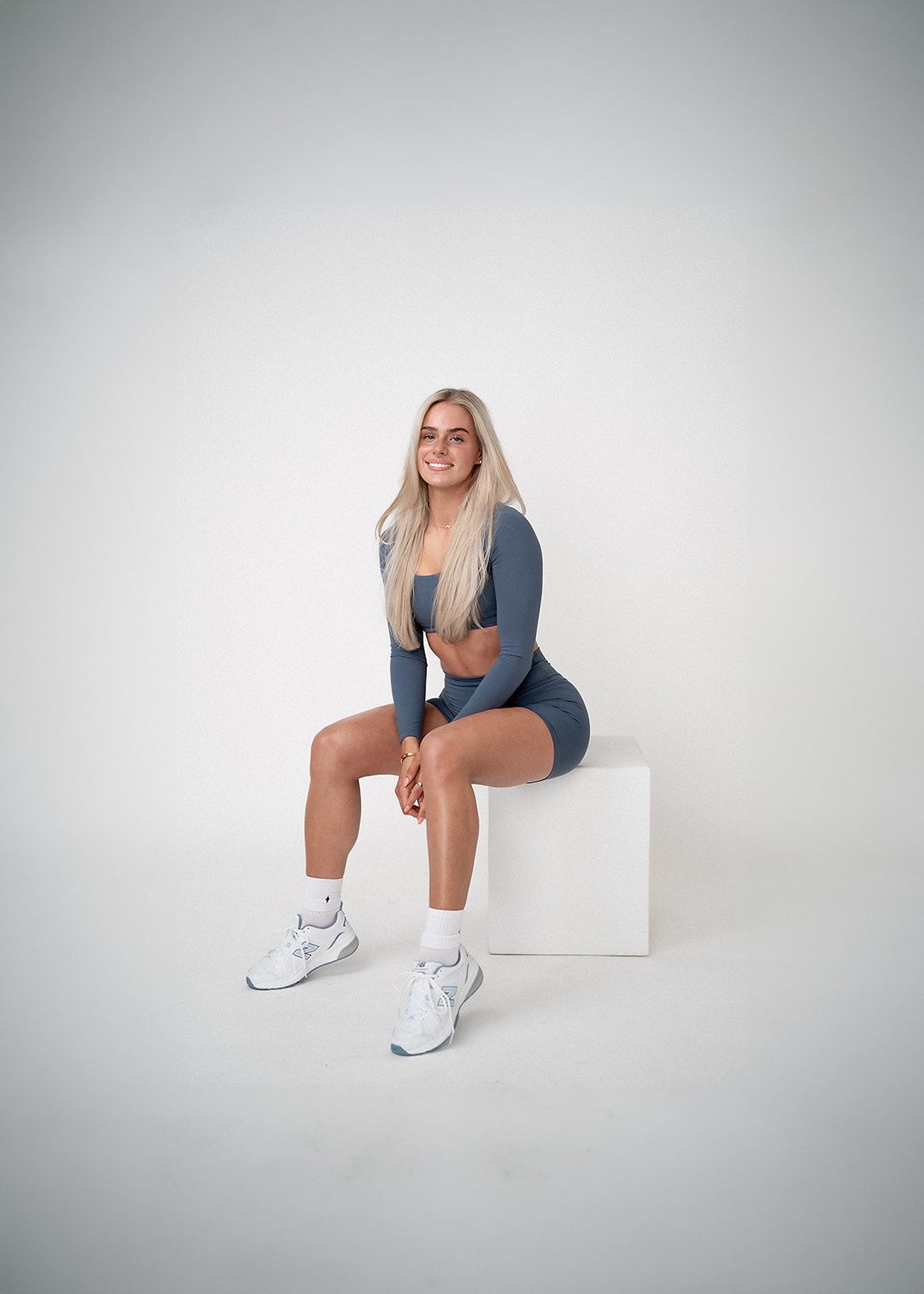 A woman is sitting on a white box on a white background.