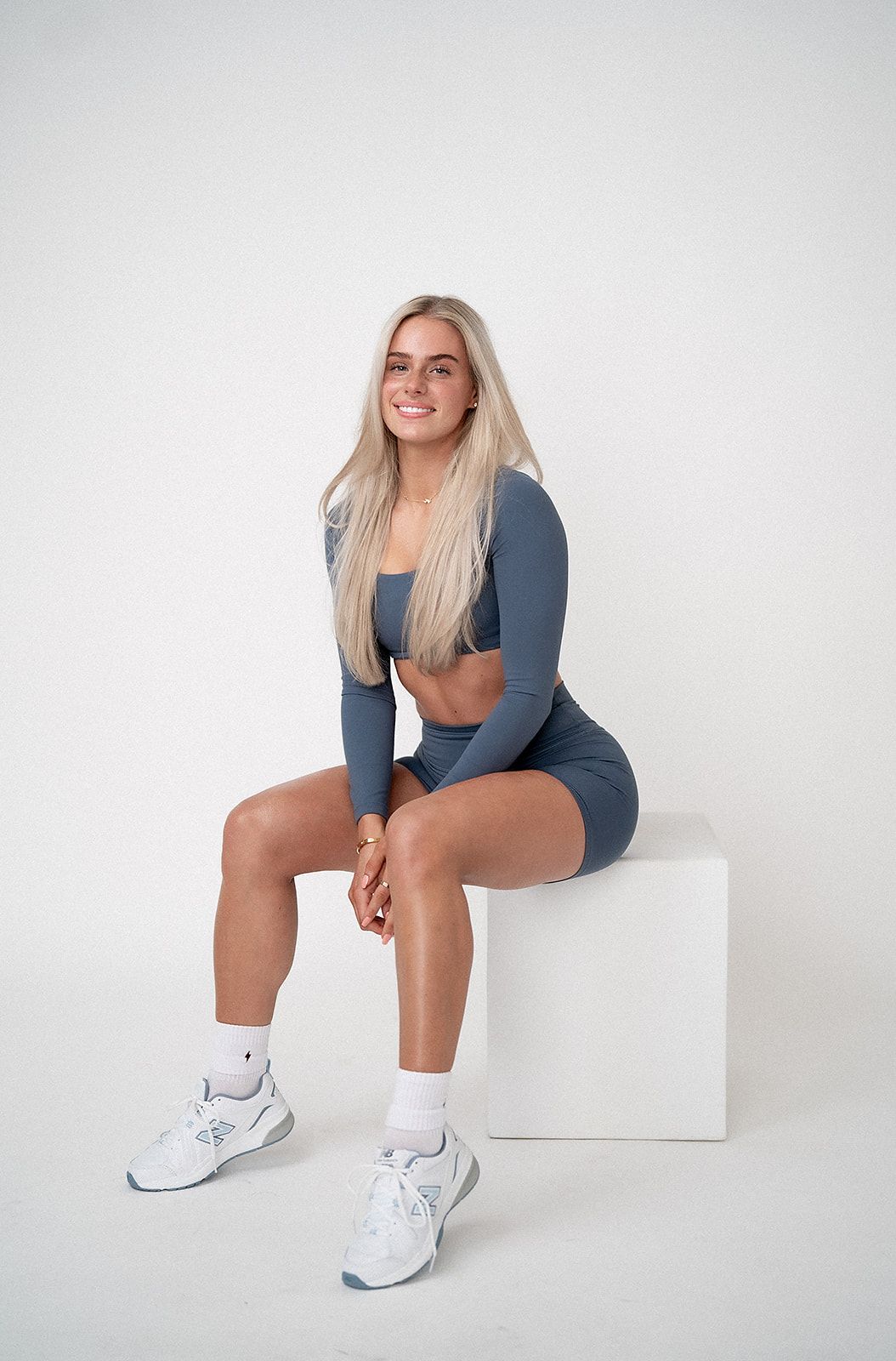A woman in a blue crop top and shorts is sitting on a white cube.