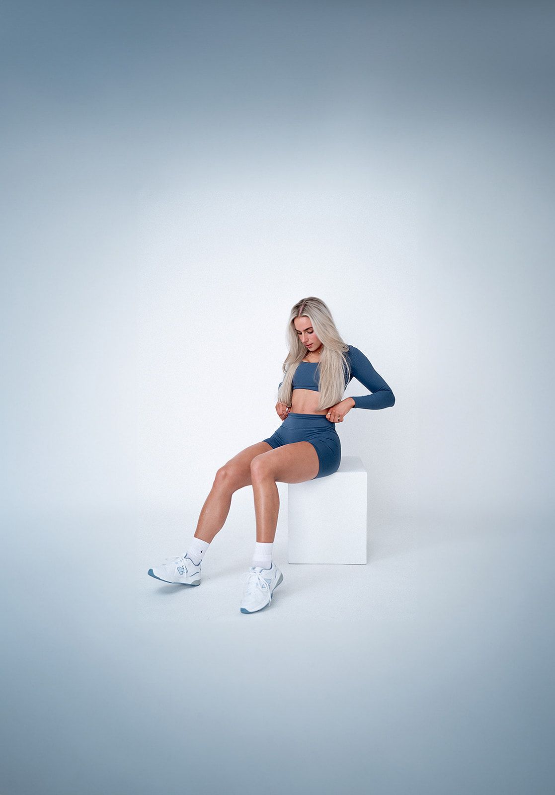 A woman is sitting on a white cube.
