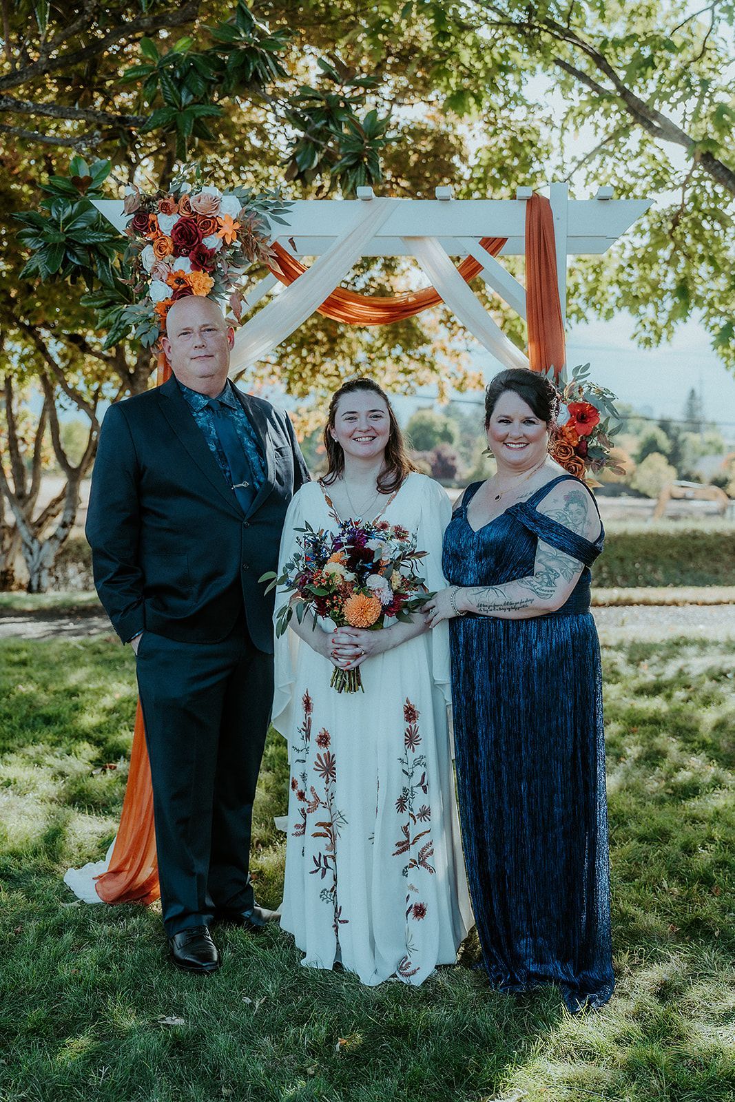 A bride, her mother and father are posing for a picture at her wedding.