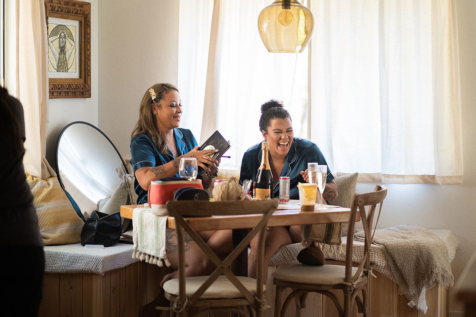 Two women are sitting at a table in a room laughing.