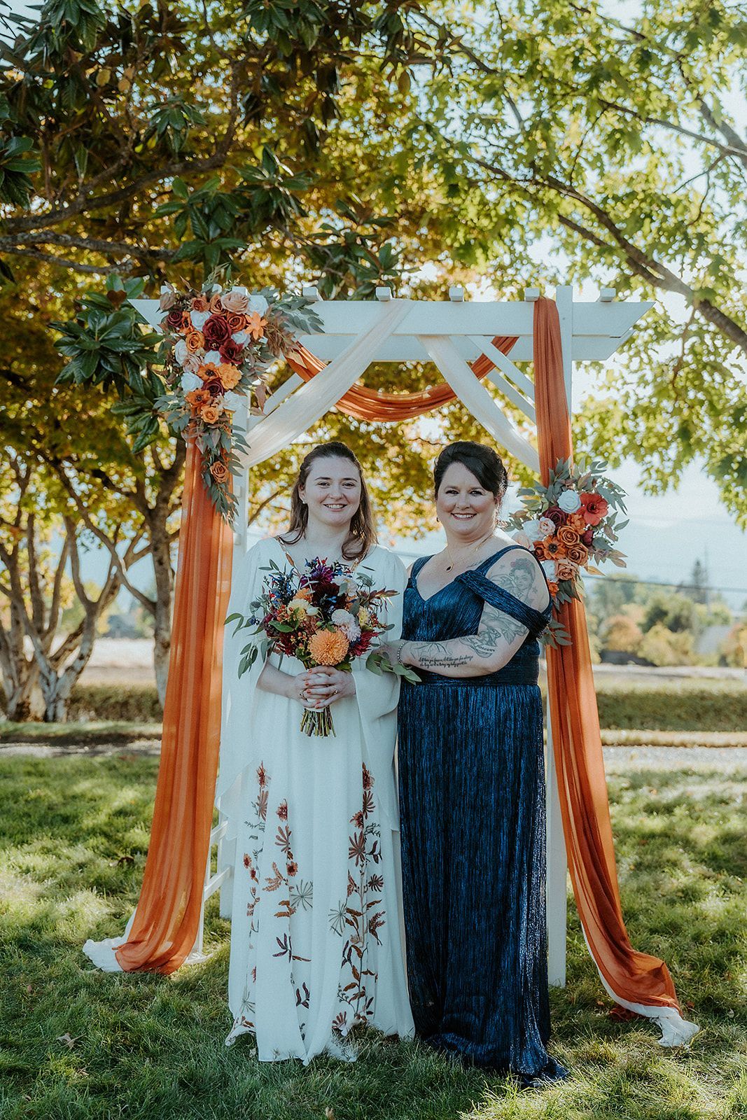 A bride and her mother are posing for a picture in front of a wedding arch.