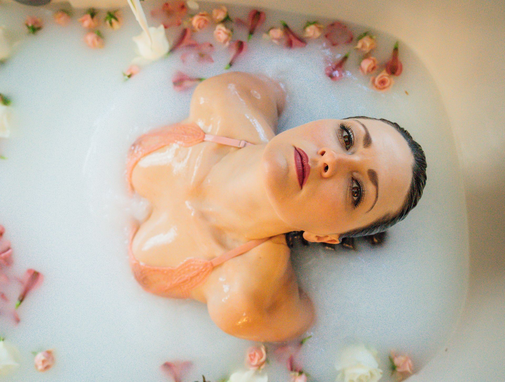 A woman in lingerie is in a mith bath with flowers.