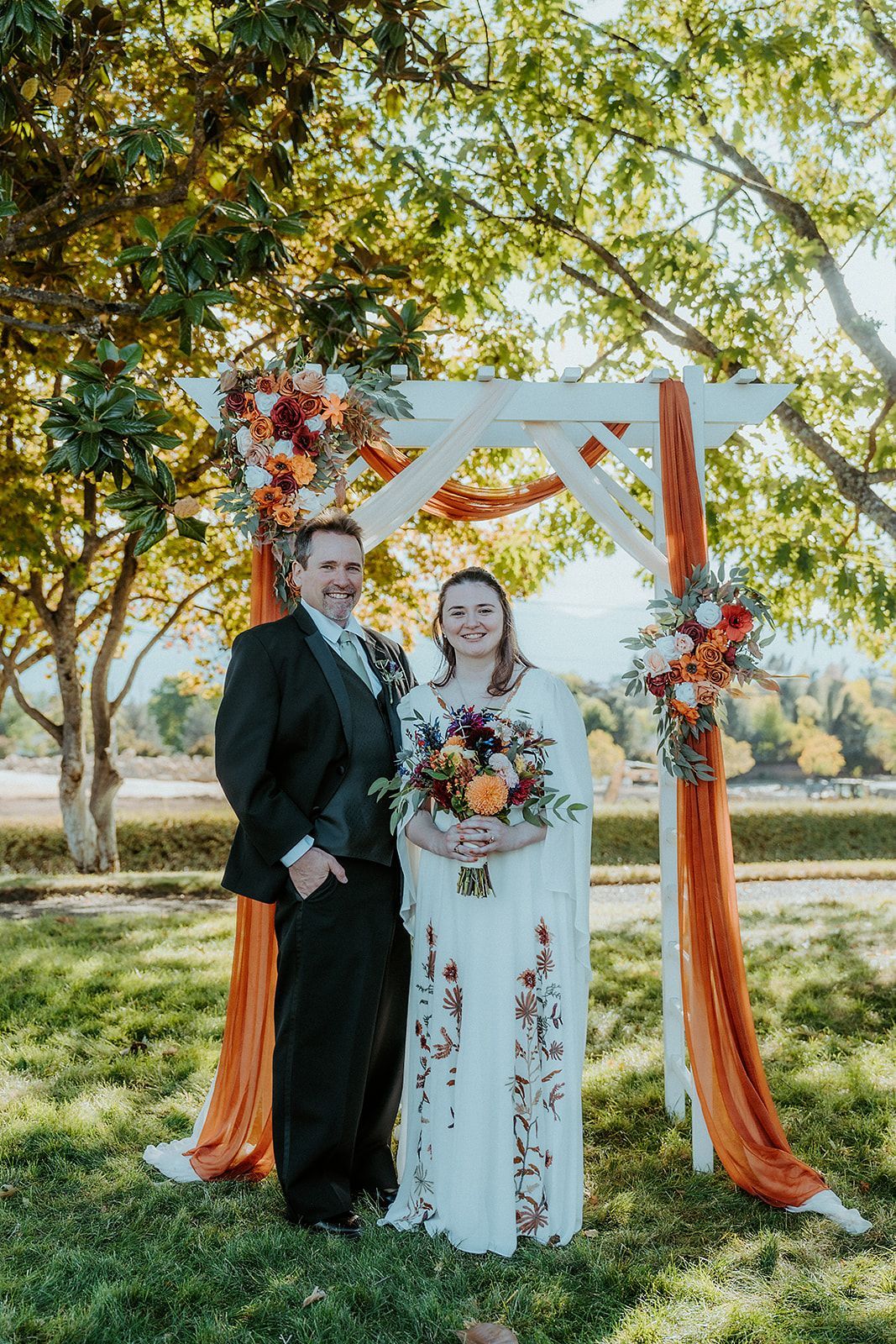 A bride and father are posing for a picture under a wedding arch.