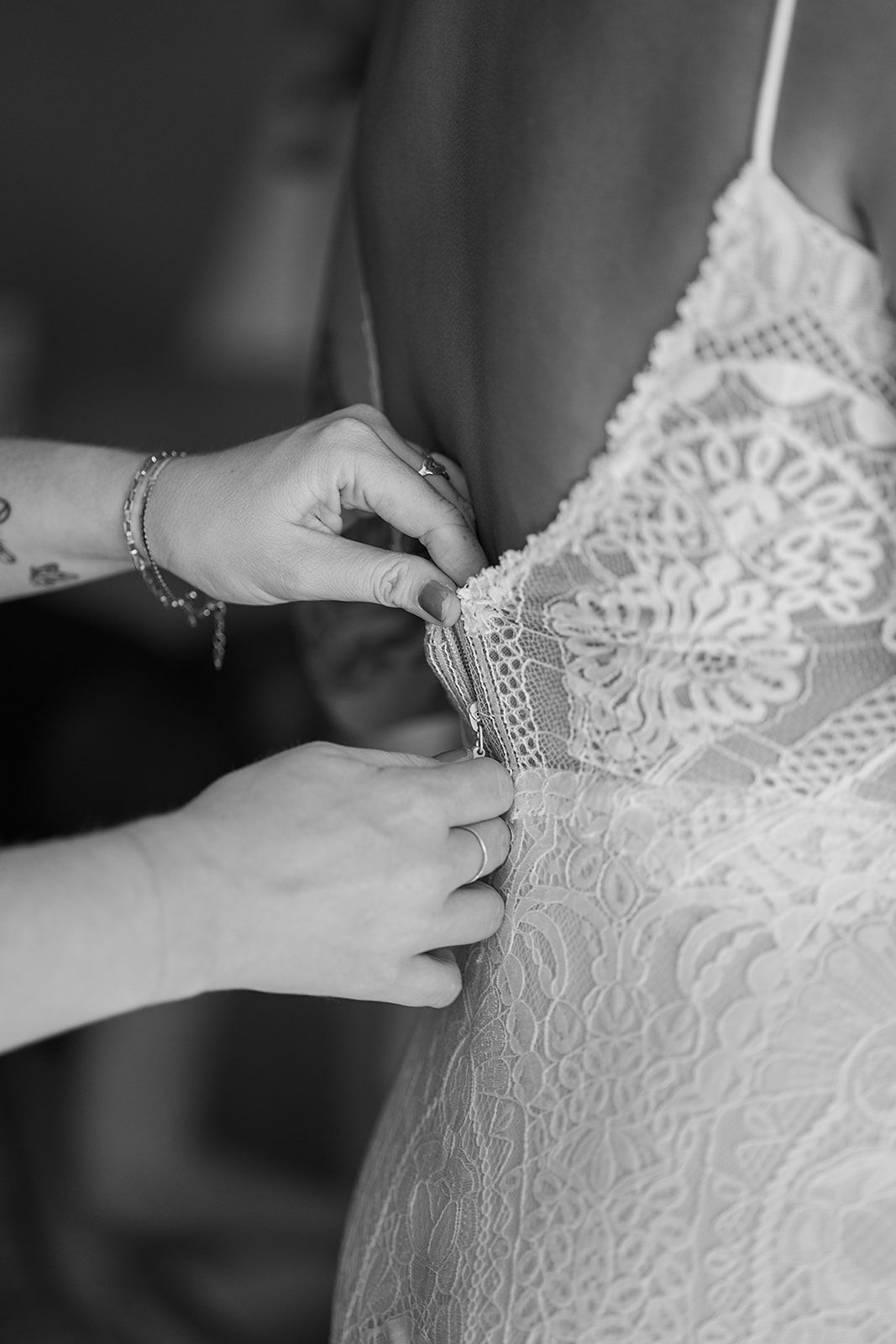 A black and white photo of a woman helping a bride get ready for her wedding.