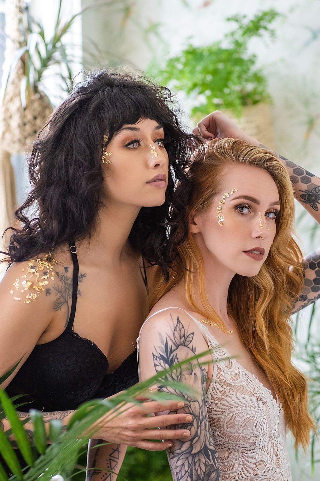 Two women are standing next to each other in front of plants.