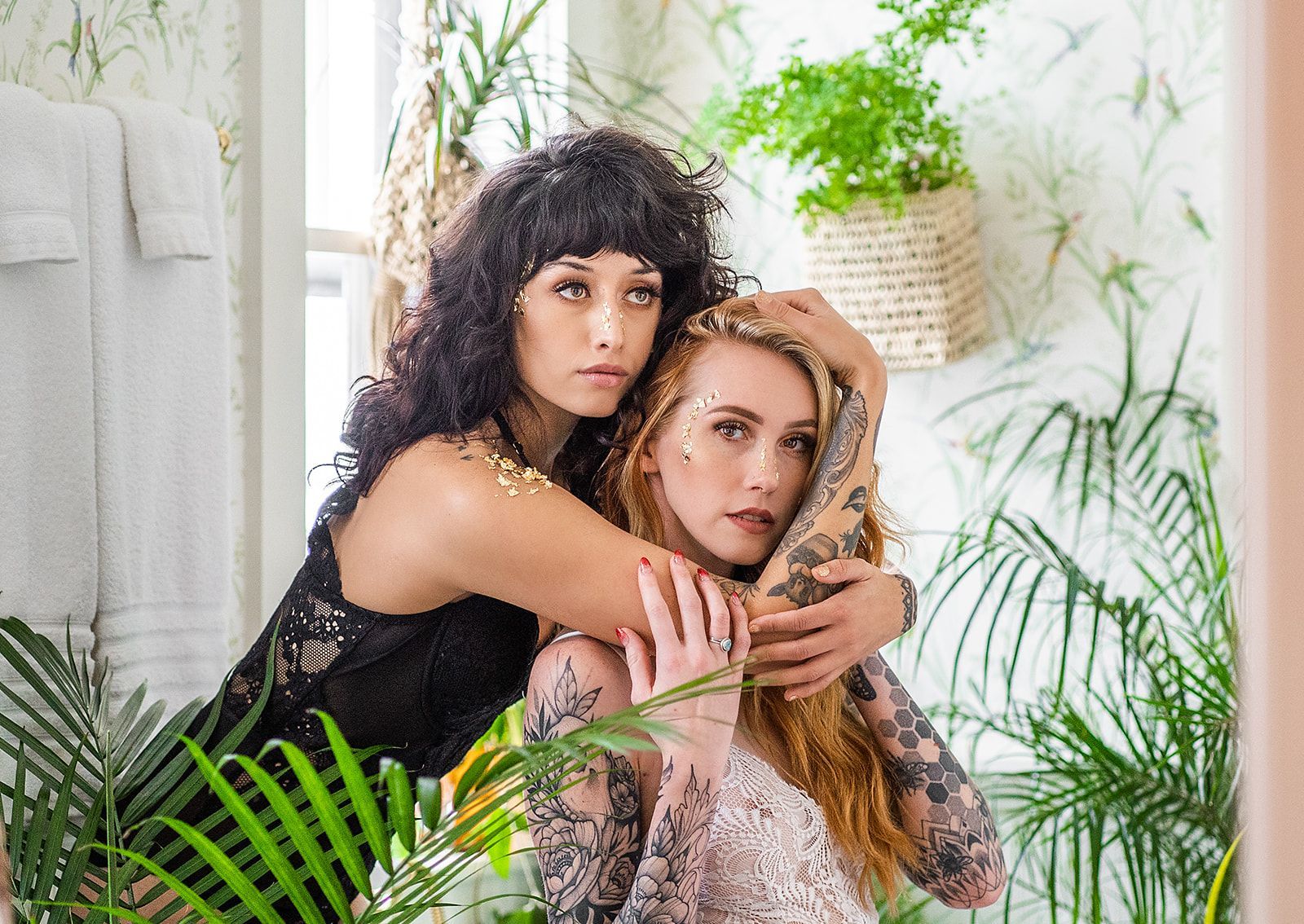 Two women are hugging each other in front of a mirror in a bathroom surrounded by plants.