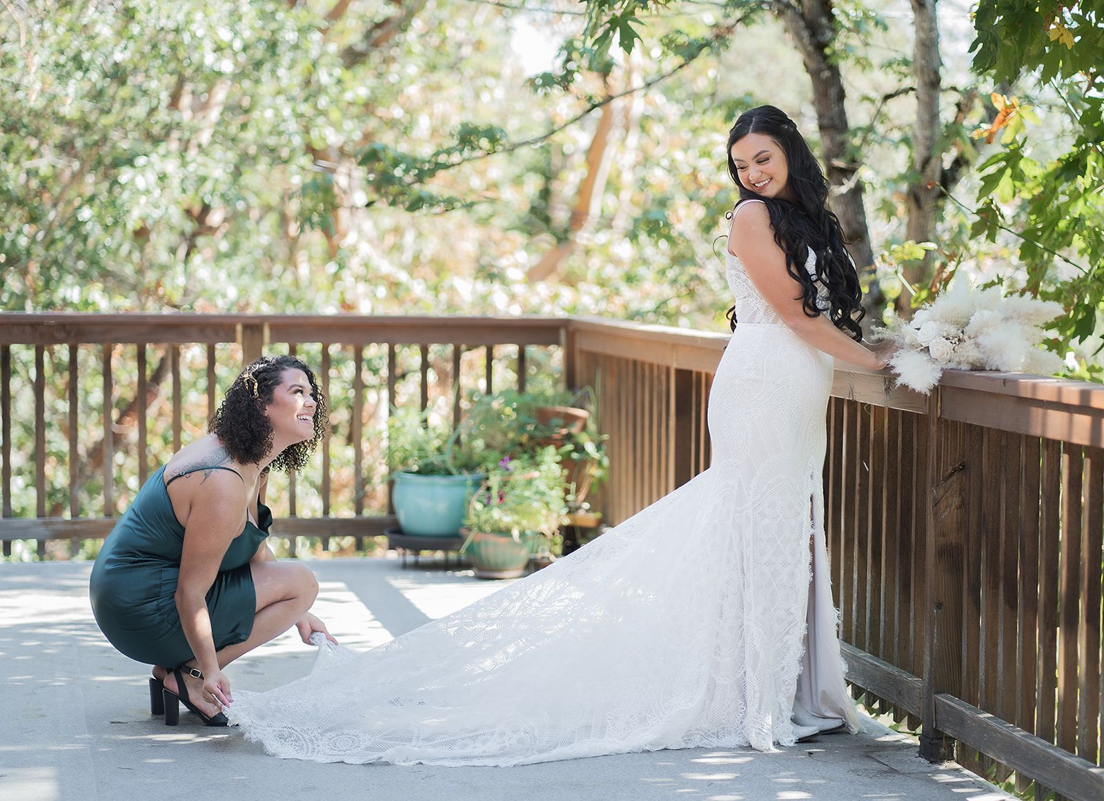 A woman is helping a bride with her wedding dress on a deck.